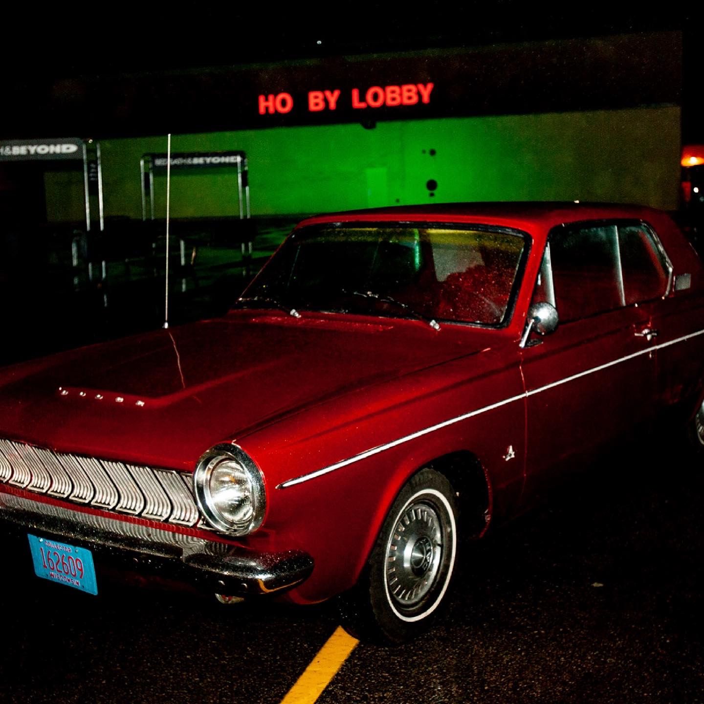 A red vintage car glowing under neon light in Sheboygan at night.