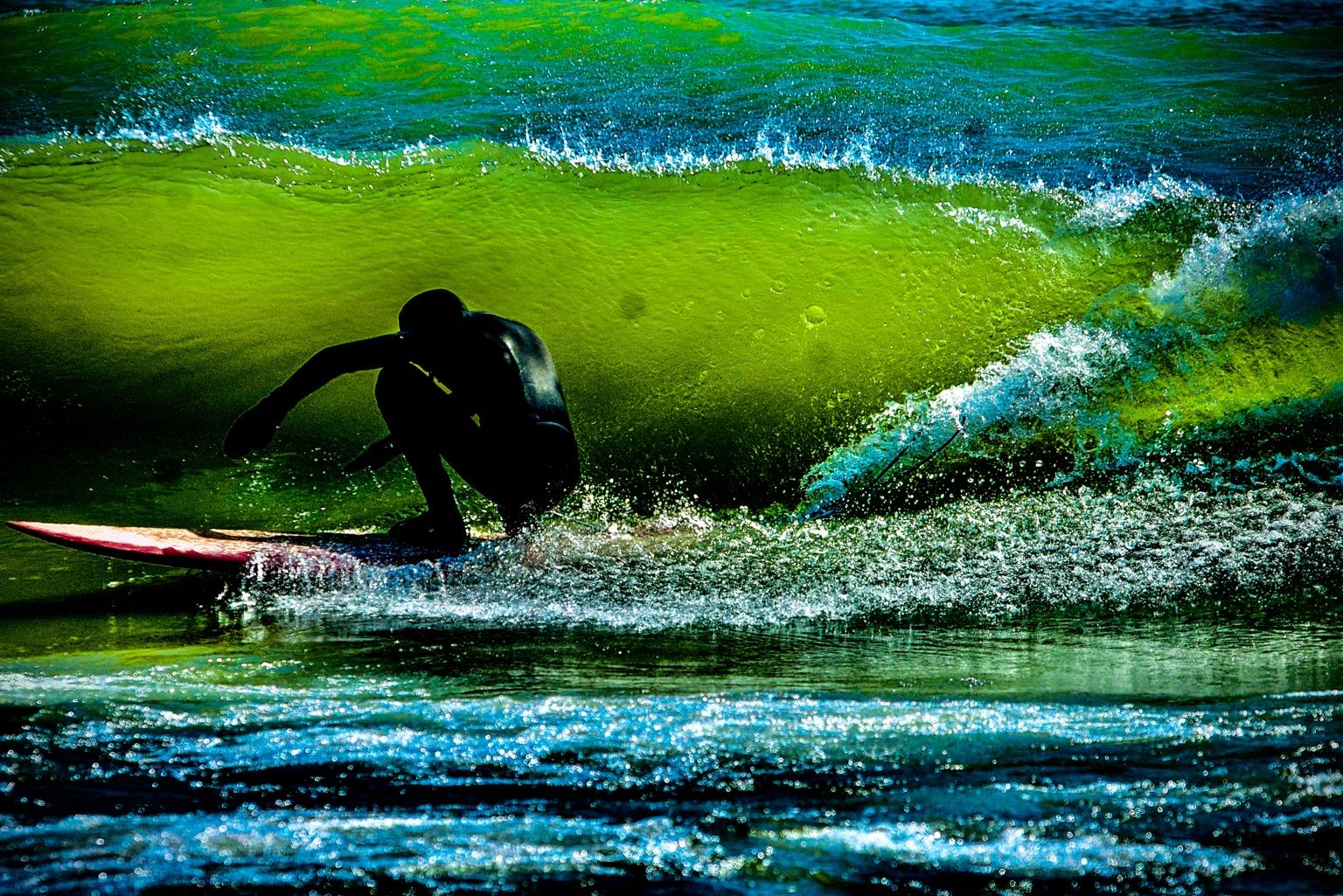 A surfer inside a vivid green-blue wave on Lake Michigan.