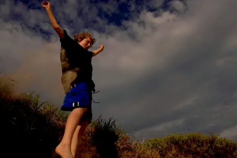 A kid leaping off a grassy dune against a dark sky at Kohler-Andrae.