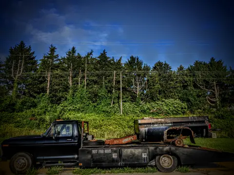 A rusted old tow rig parked against a wall of pines. Stenciled on the side: NOT FOR HIRE.