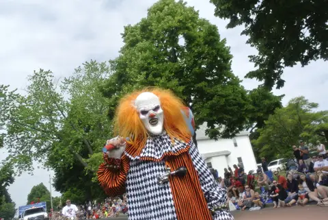 An orange-wigged, checkered clown works the curb.
