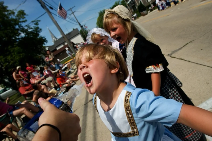 Kid catching a squirted stream of water at the parade