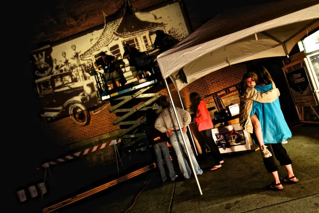 Walldogs at night under a work tent, sketching mural outlines.