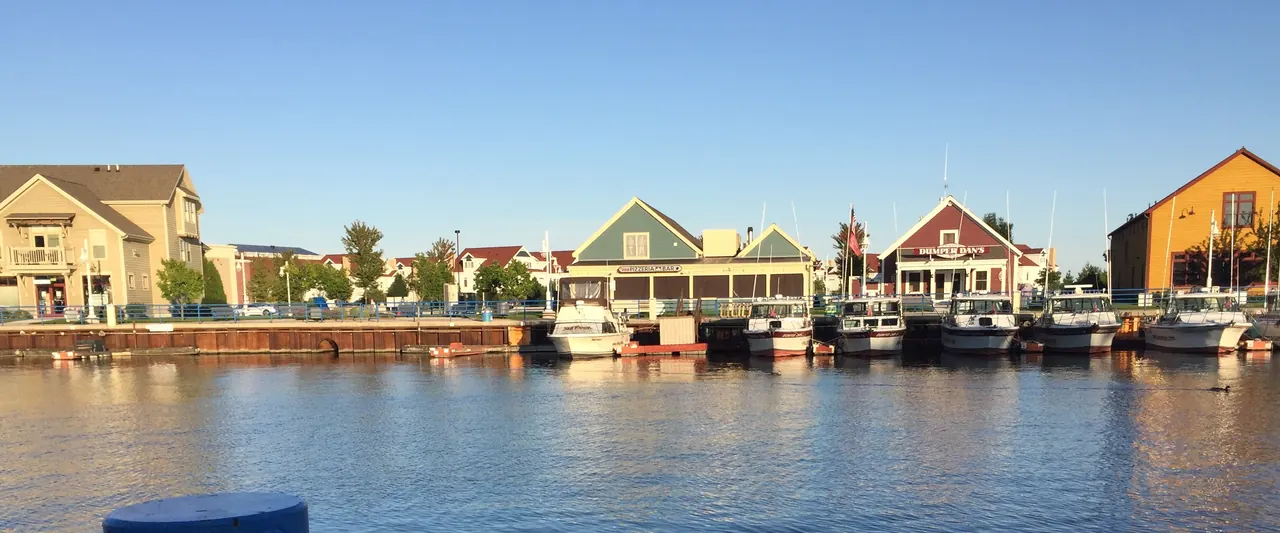 The Harbor Centre Marina boardwalk across the water in 2016: a row of docked white boats in front of colorful waterfront buildings. No people in the photo.
