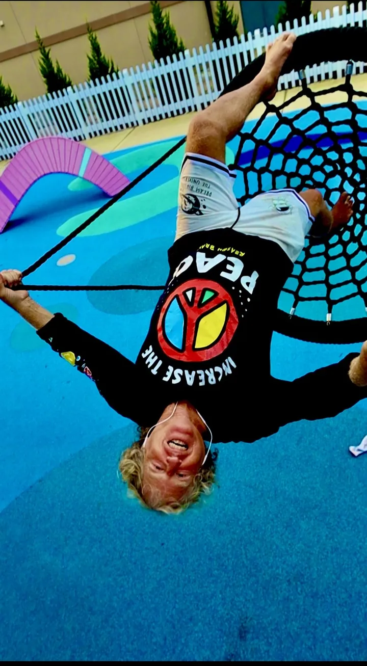 Mike Brunette hanging upside down on a rope web swing, laughing