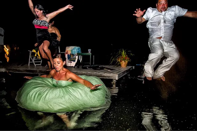Wedding night dock jump at Elkhart Lake, bride in green dress already in the water, groom mid-air